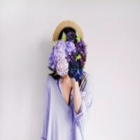 Frau versteckt ihr Gesicht hinter Blumen